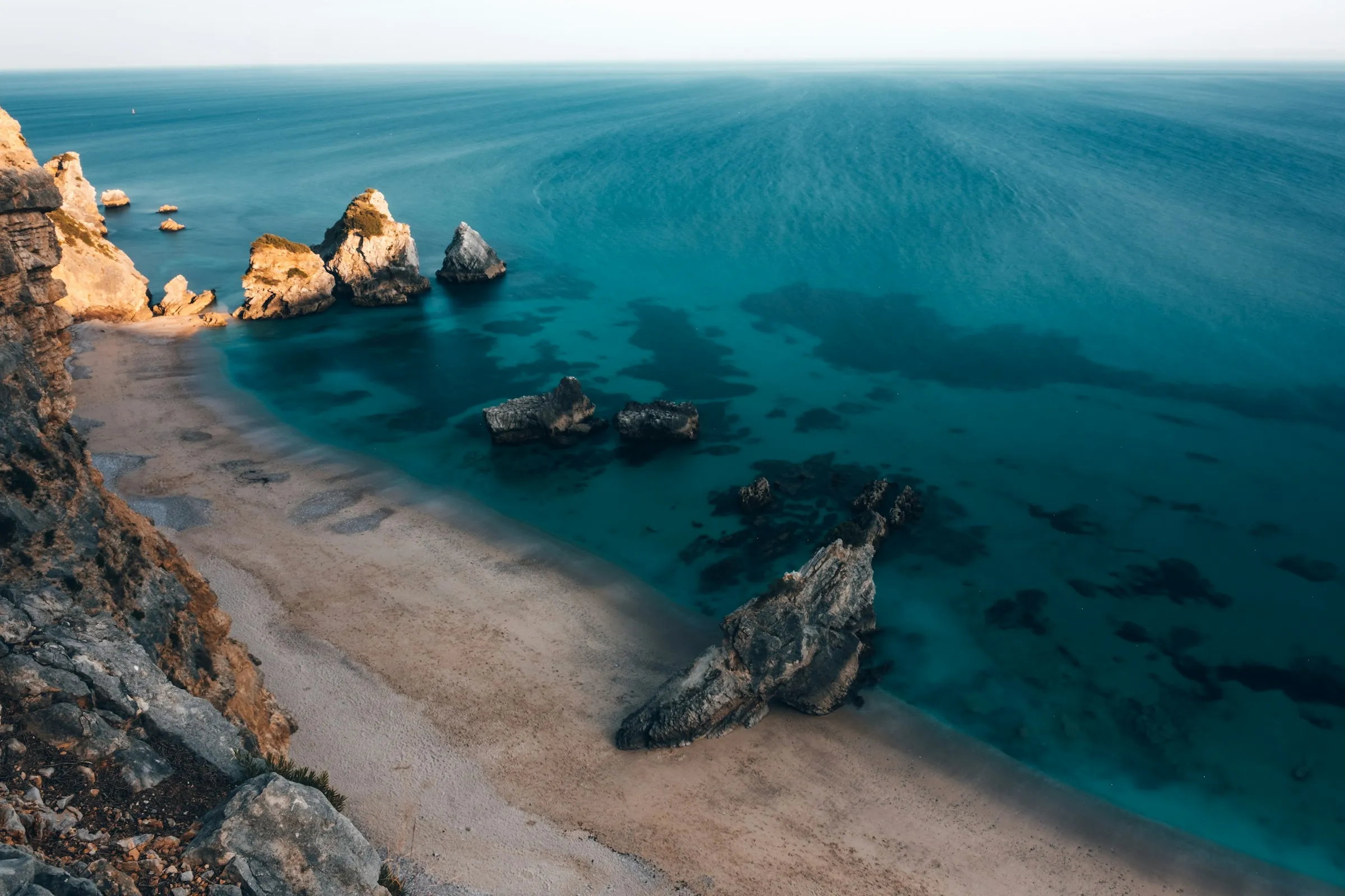 Aerial view of a secluded beach cove, turquoise water meeting a sandy shore beneath sea cliffs