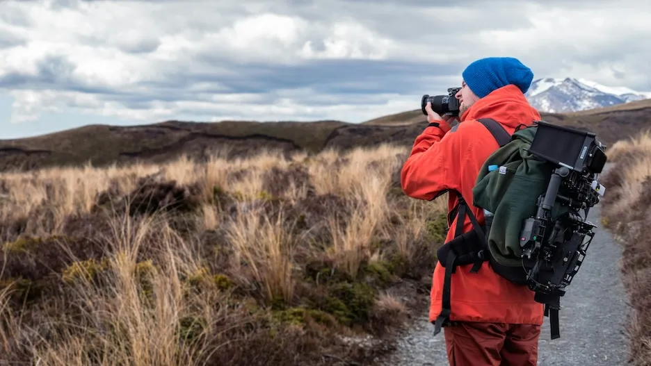 A photographer in a red jacket shooting with a telephoto lens on a windswept moorland trail.